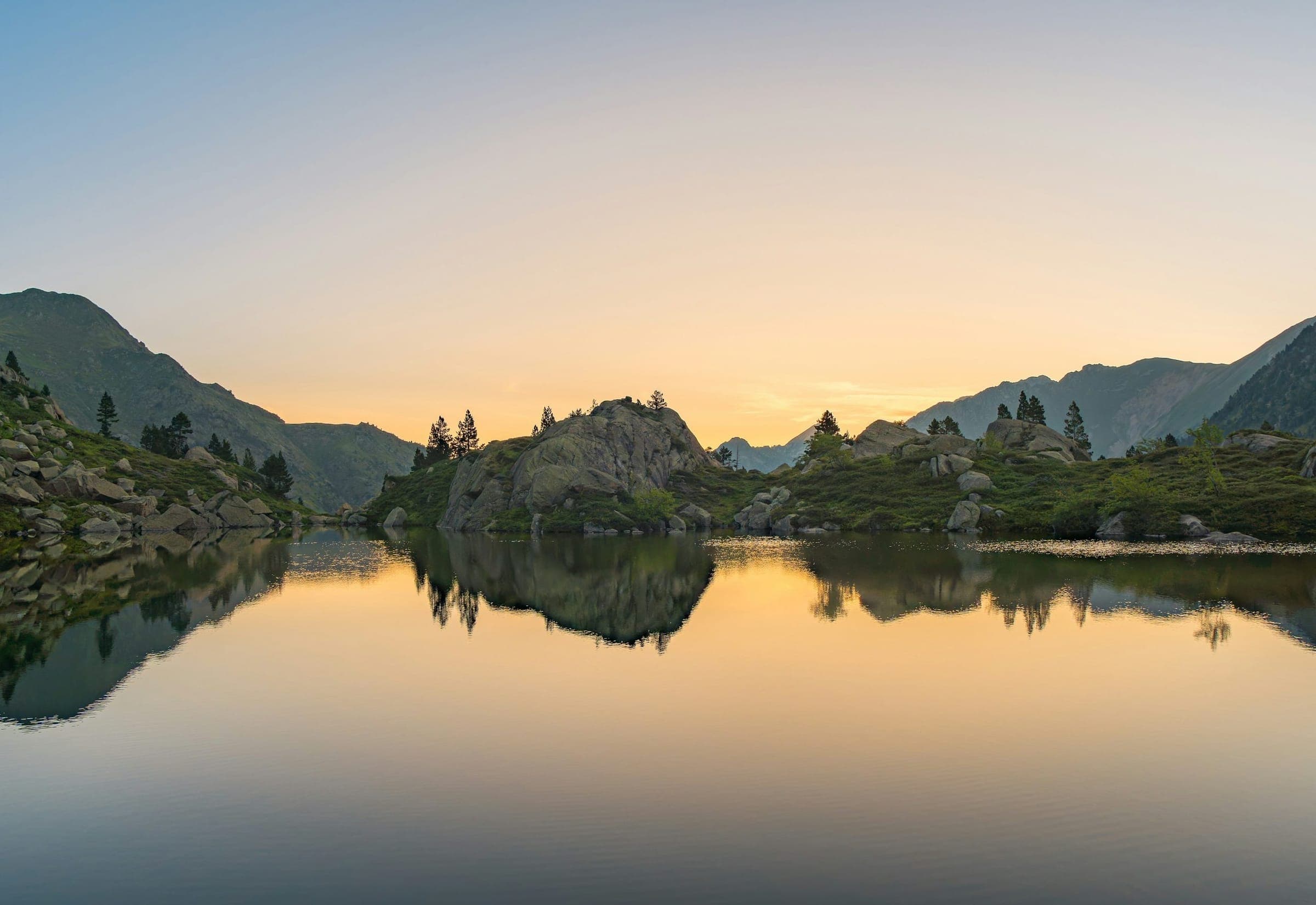 A mountain lake at dawn, its wooded islets mirrored in still water